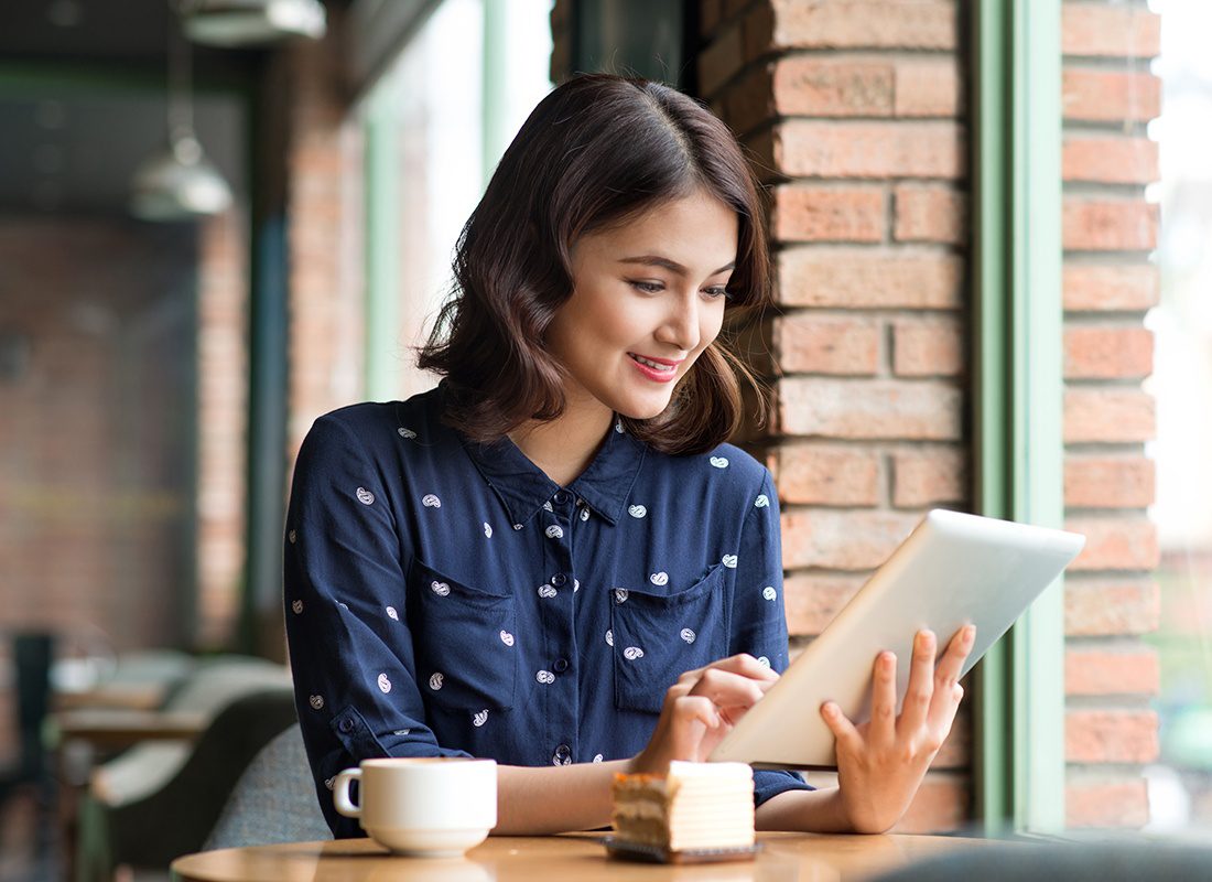 Read Our Reviews - Young Woman Reading a Tablet at a Cafe